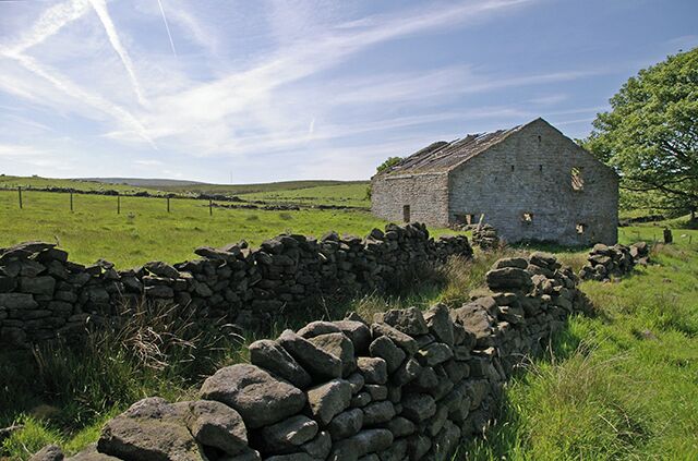 A stone wall, a stone building, and a grassy field.