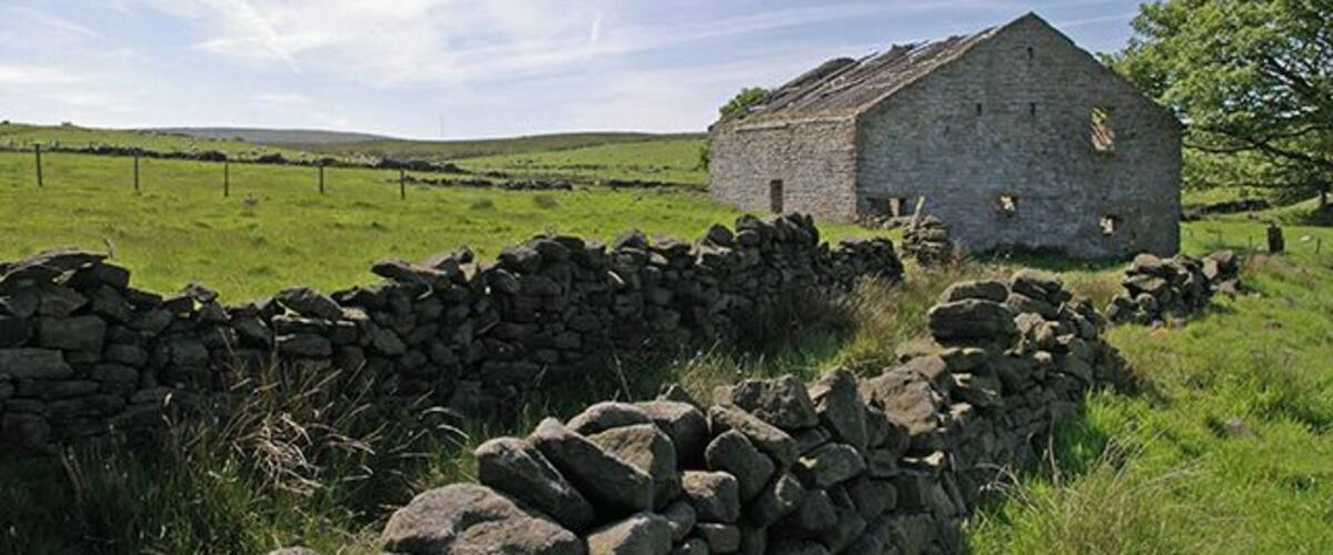 A stone wall, a stone building, and a grassy field.