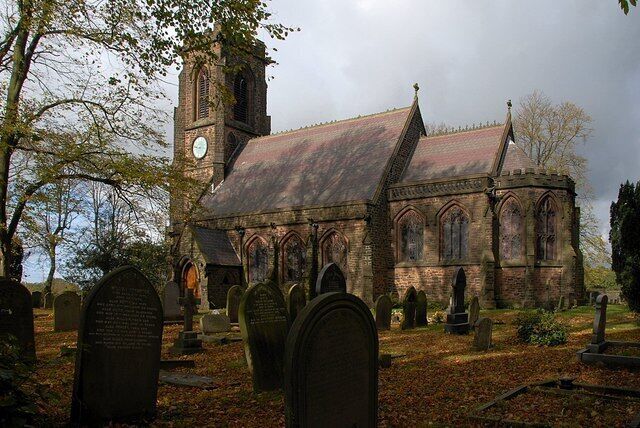 A church with a clock tower, surrounded by gravestones and trees.
