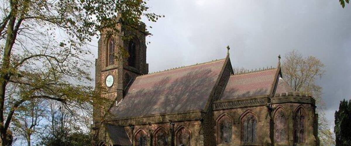 A church with a clock tower, surrounded by gravestones and trees.