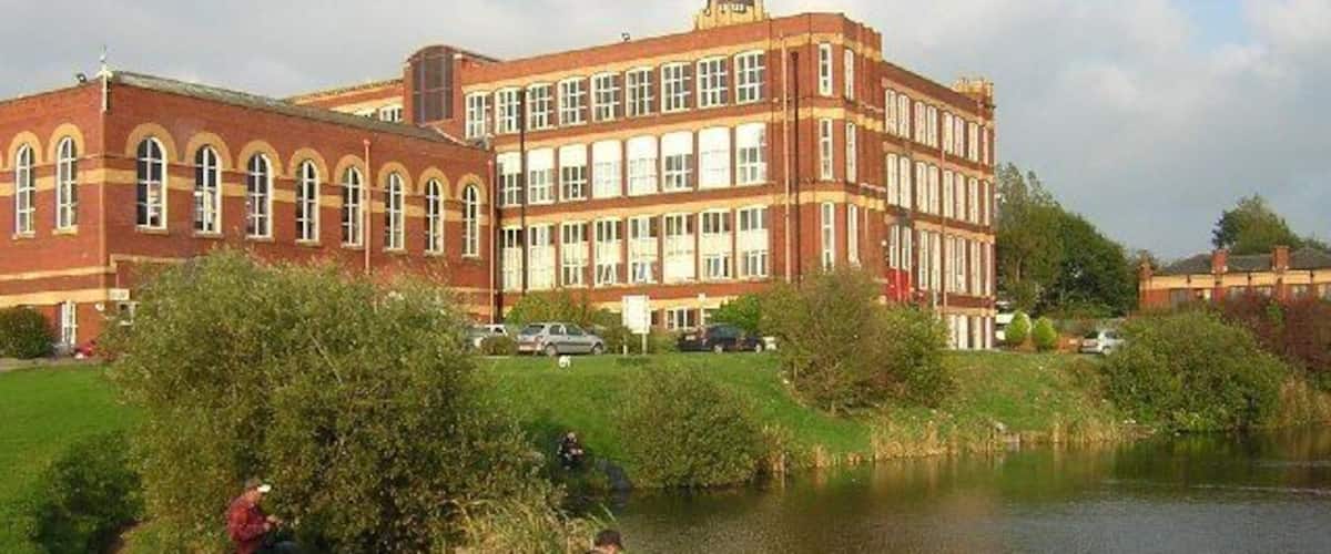 A large red brick building with arched windows and a pond in the foreground.