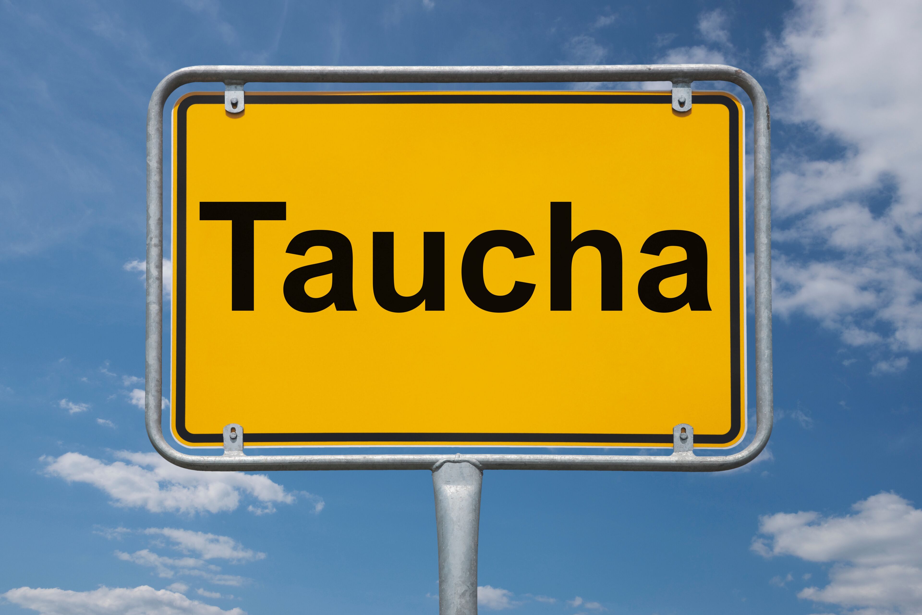 A yellow sign with the word "Taucha" against a blue sky with clouds.