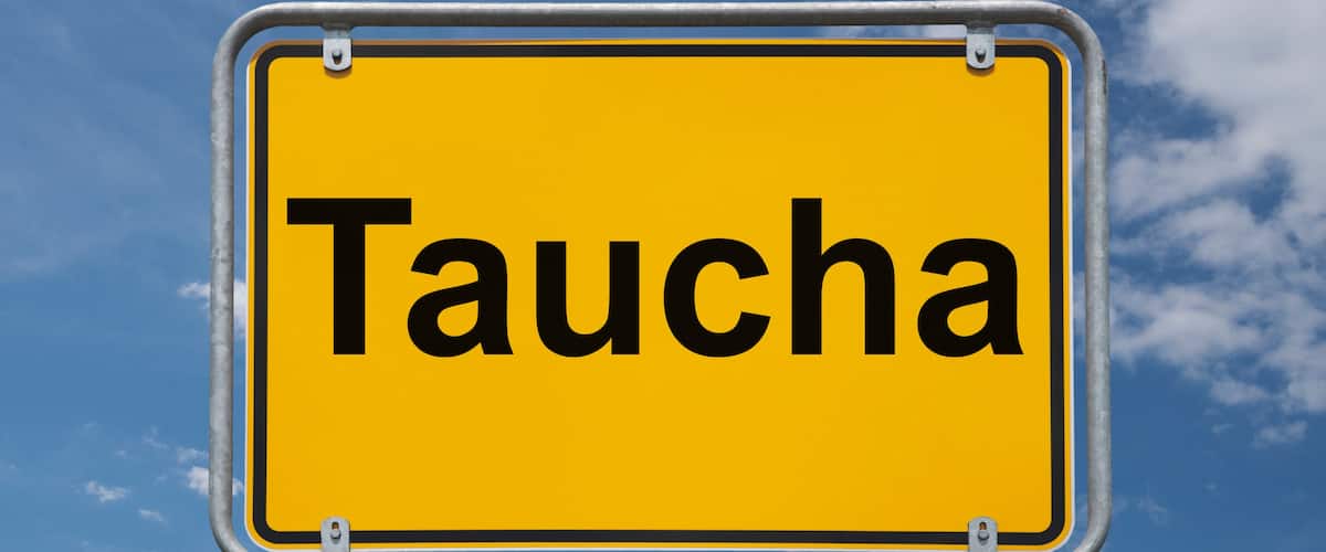 A yellow sign with the word "Taucha" against a blue sky with clouds.