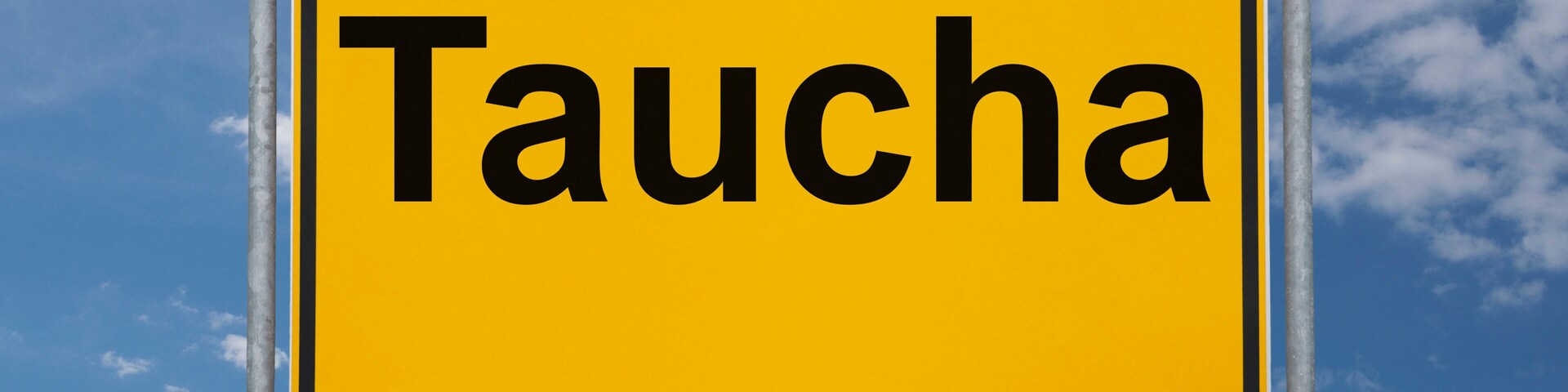 A yellow sign with the word "Taucha" against a blue sky with clouds.