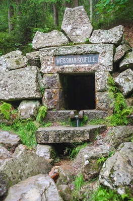 Eine Steinstruktur mit einem Schild, auf dem „WEISSMANSOUELLE“ steht, und einem kleinen Wasserhahn.