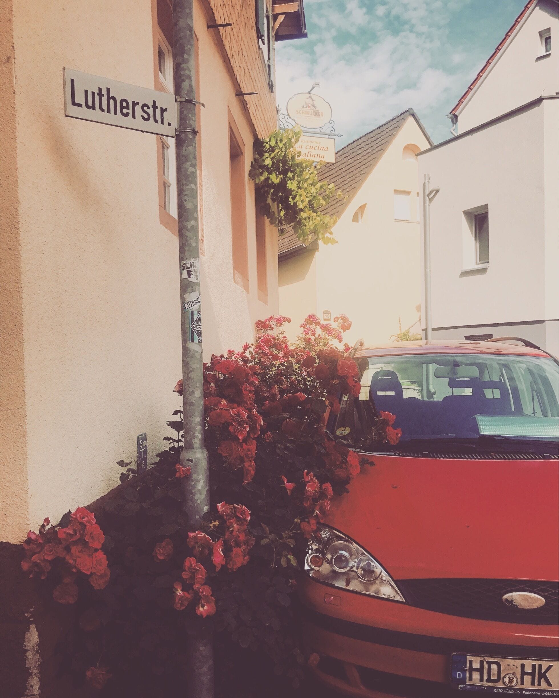 A red car parked on a street with a sign reading "Lutherstr." and a building with a sign that says "Schmucker."