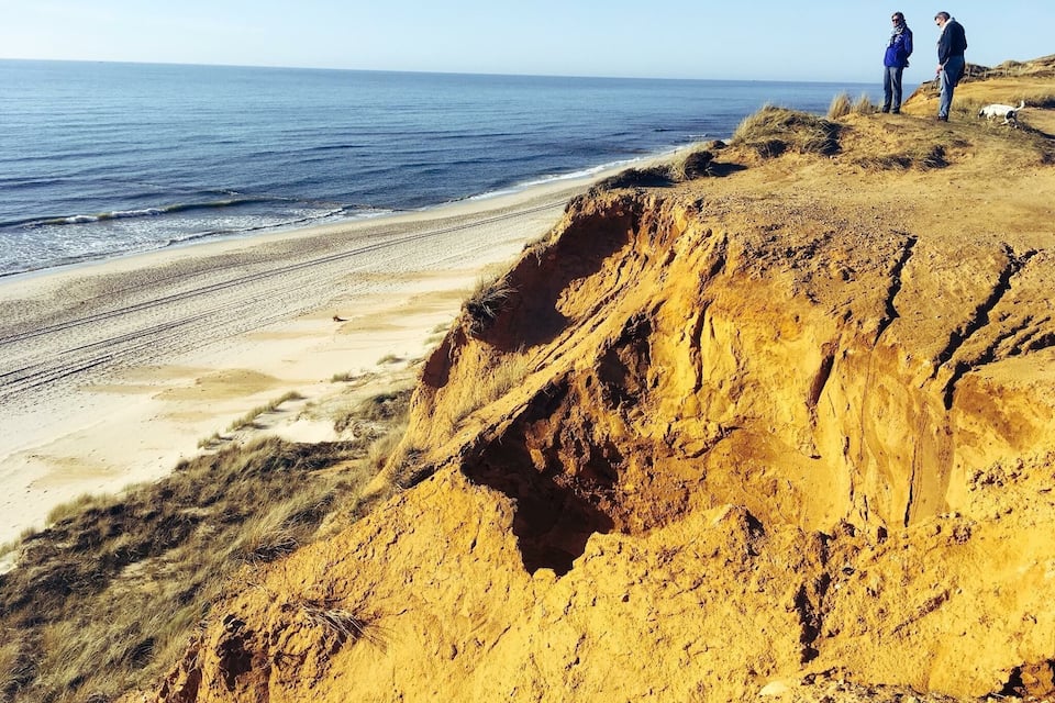 A coastal cliff with a sandy beach and the ocean.