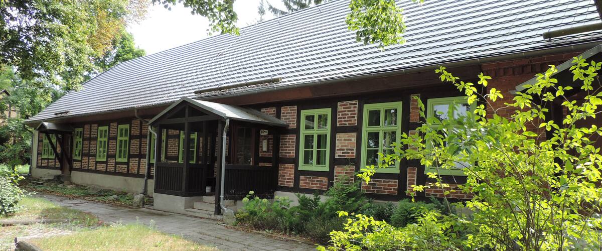 A traditional building with green window frames and a brick facade, surrounded by trees and a grassy area.