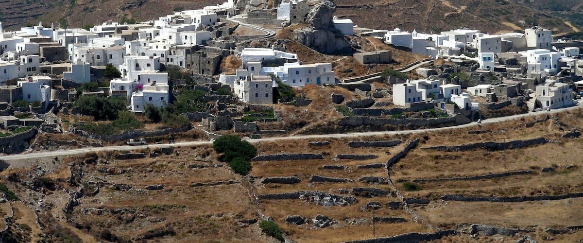 Un pueblo encalado con casas de piedra, situado en una ladera, con vistas a una escarpada cadena montañosa y al mar.