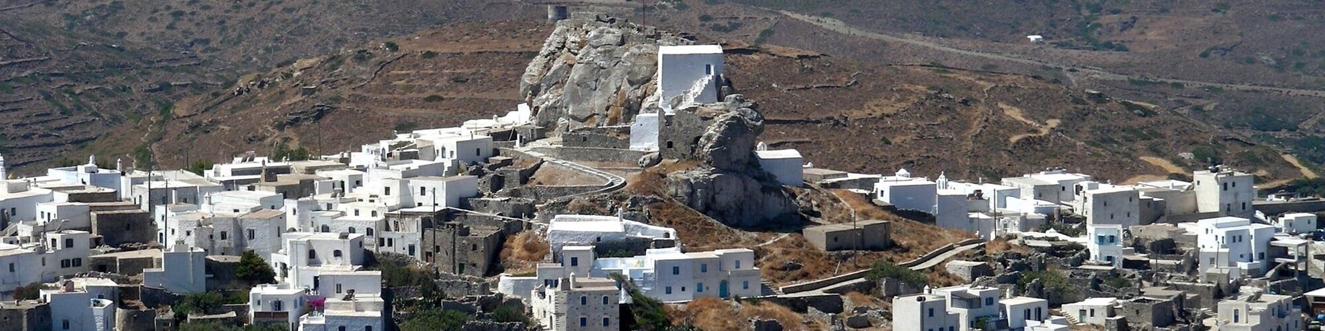 Un pueblo encalado con casas de piedra, situado en una ladera, con vistas a una escarpada cadena montañosa y al mar.