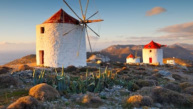 Um moinho de vento, um edifício branco com telhado vermelho e uma paisagem montanhosa.