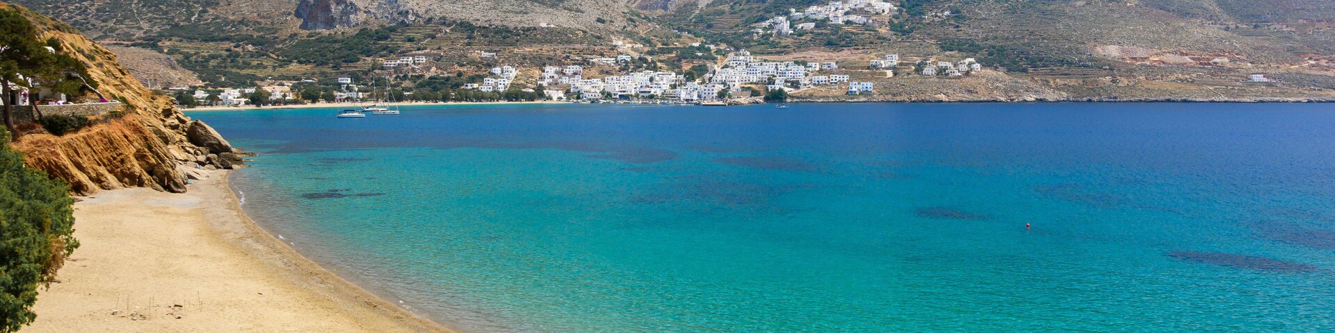 A coastal landscape with a sandy beach, clear turquoise waters, and a mountainous backdrop.