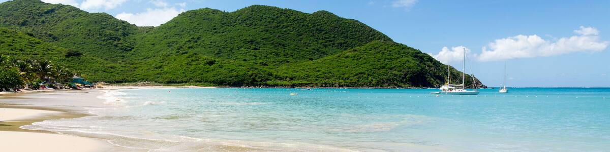 A beach with clear turquoise water, a sandy shore, and lush green hills in the background.