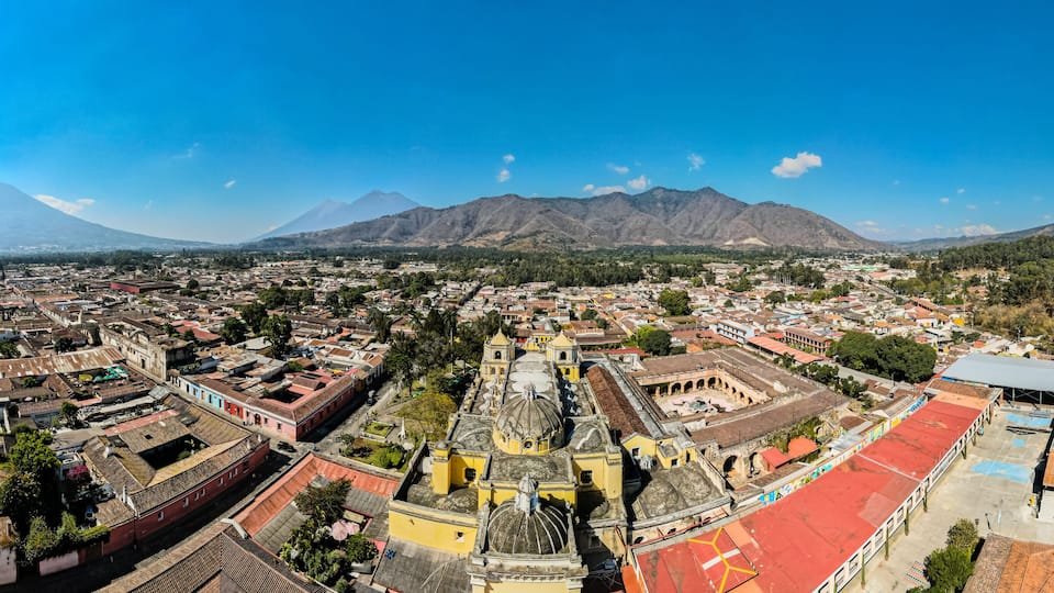 A cityscape with a prominent church, a large volcano in the background, and surrounding greenery.