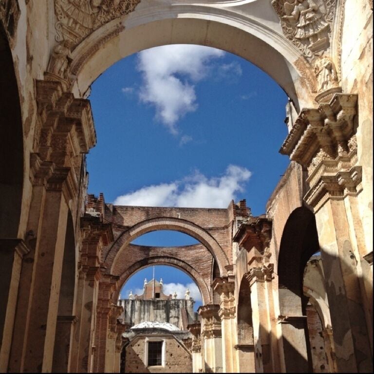 An arched corridor with intricate stone carvings and a clear blue sky above.