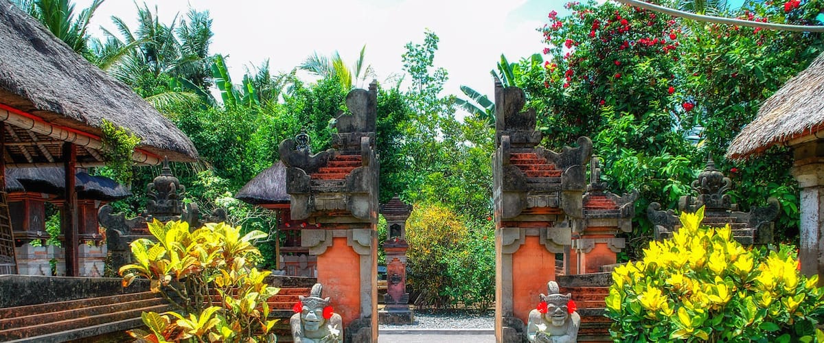 A traditional Balinese temple entrance with ornate stone statues and thatched-roof structures.