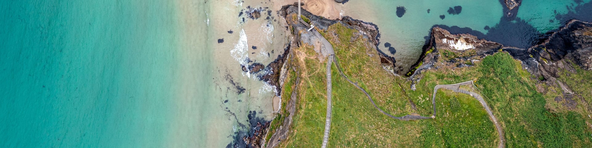 A coastal landscape with a beach, rocky cliffs, and a small building near the shore.