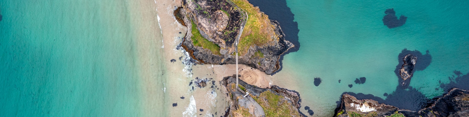 Un paisaje costero con playa, acantilados rocosos y un pequeño edificio cerca de la orilla.