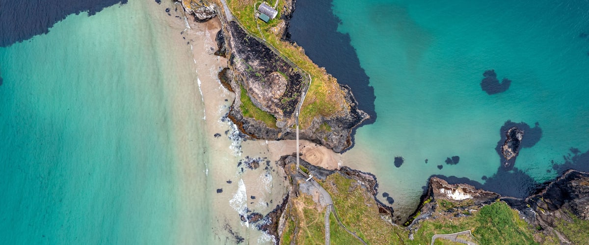 A coastal landscape with a beach, rocky cliffs, and a small building near the shore.