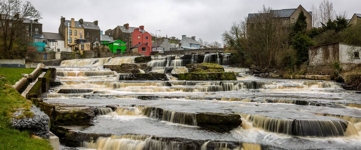 A multi-tiered waterfall with a town in the background.