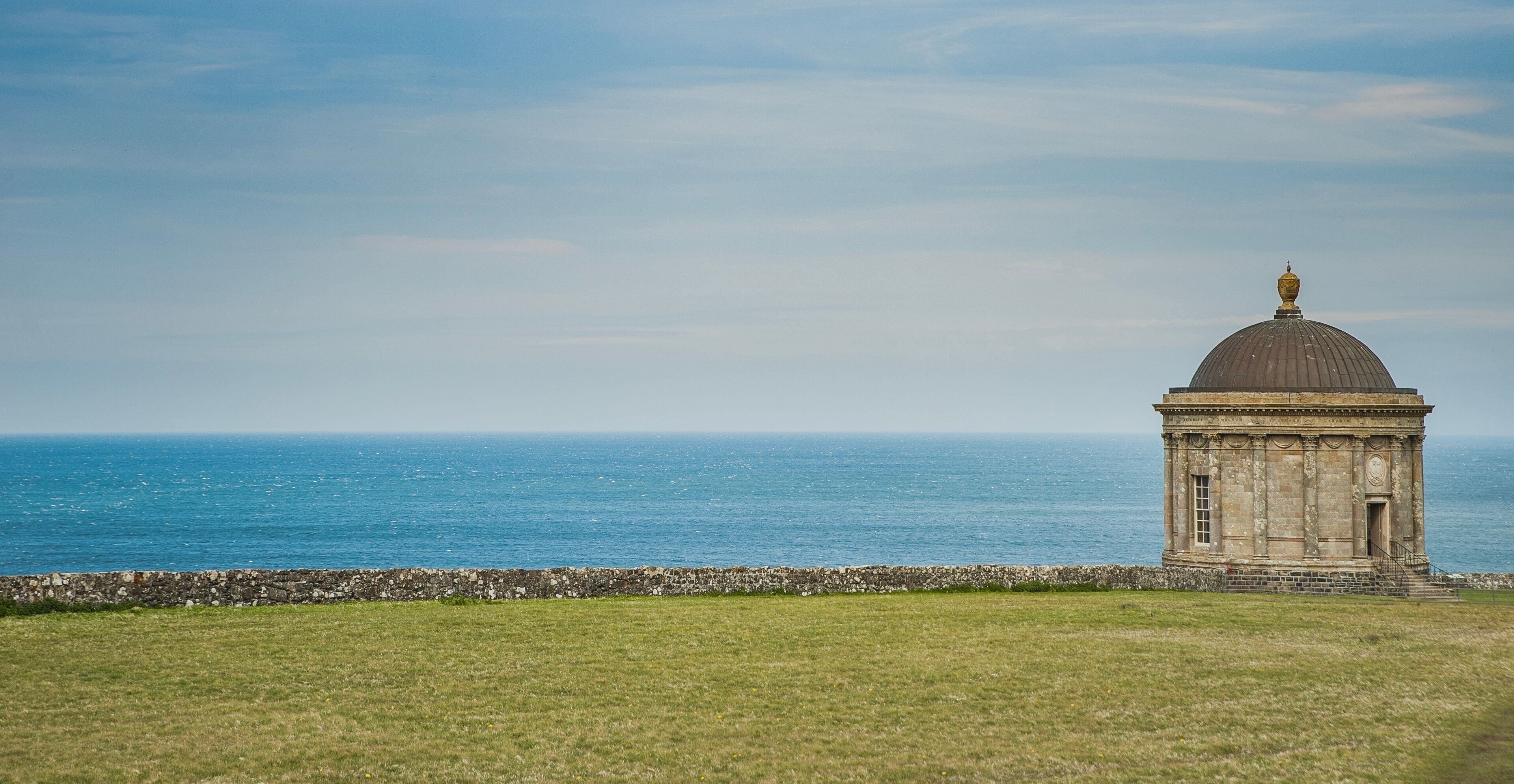 Historical round temple on the verge of a cliff overlooking blue ocean 's infinity. Touristic Irish cultural heritage with a circular chapel or tabernacle by the sea in Castlerock, Northern Ireland