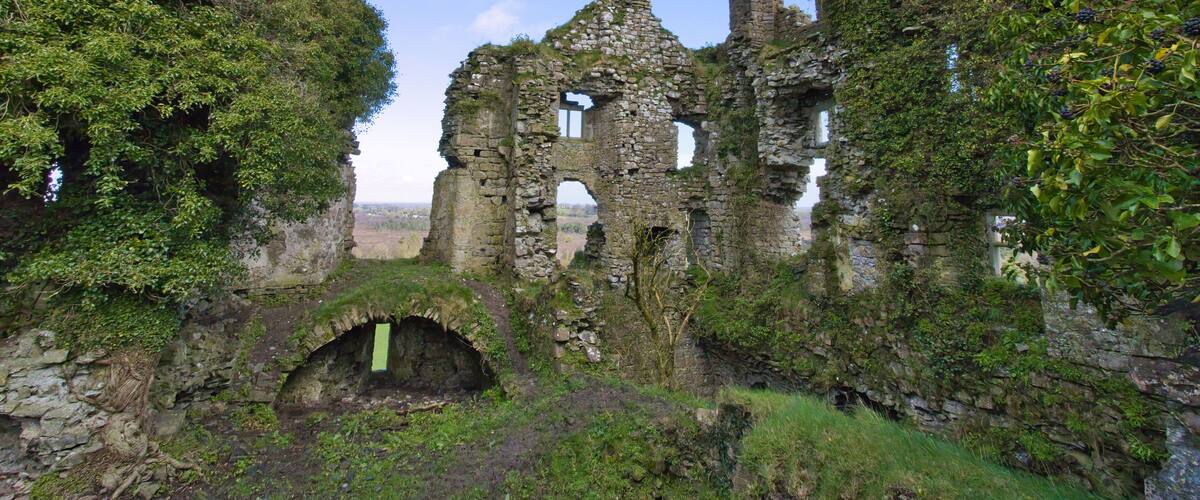 A historic stone ruin with ivy-covered walls and a small arched entrance, surrounded by lush greenery.