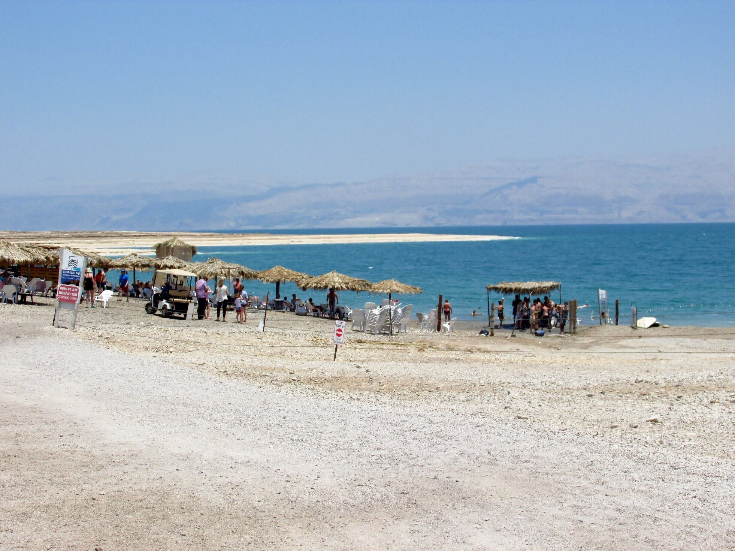 A beach with thatched umbrellas, people, and a clear blue sea.