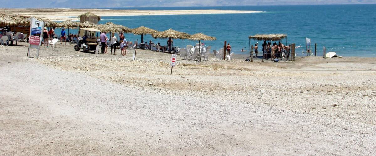 A beach with thatched umbrellas, people, and a clear blue sea.