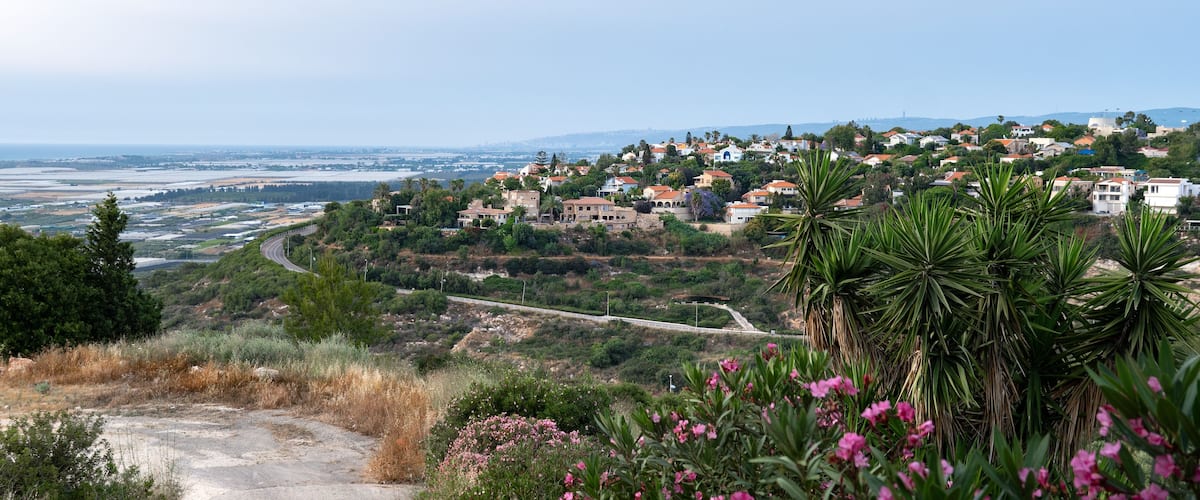 Charming coastal village with red-roof houses nestled on a hillside, overlooking farmland, the sea, and vibrant summer flora. Panoramic view. Zikhron Ya'akov, Israel.