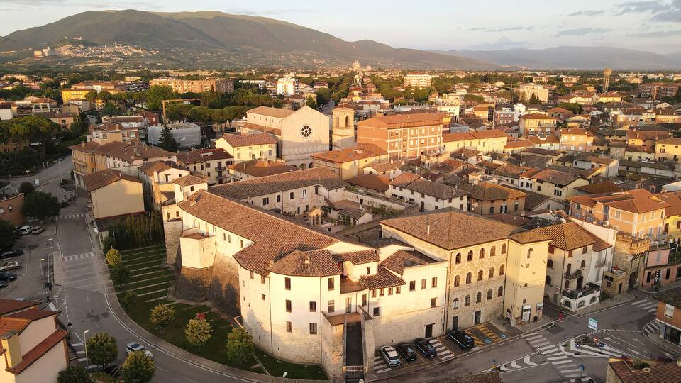 A historic town with a prominent church, a round tower, and a mountainous backdrop.