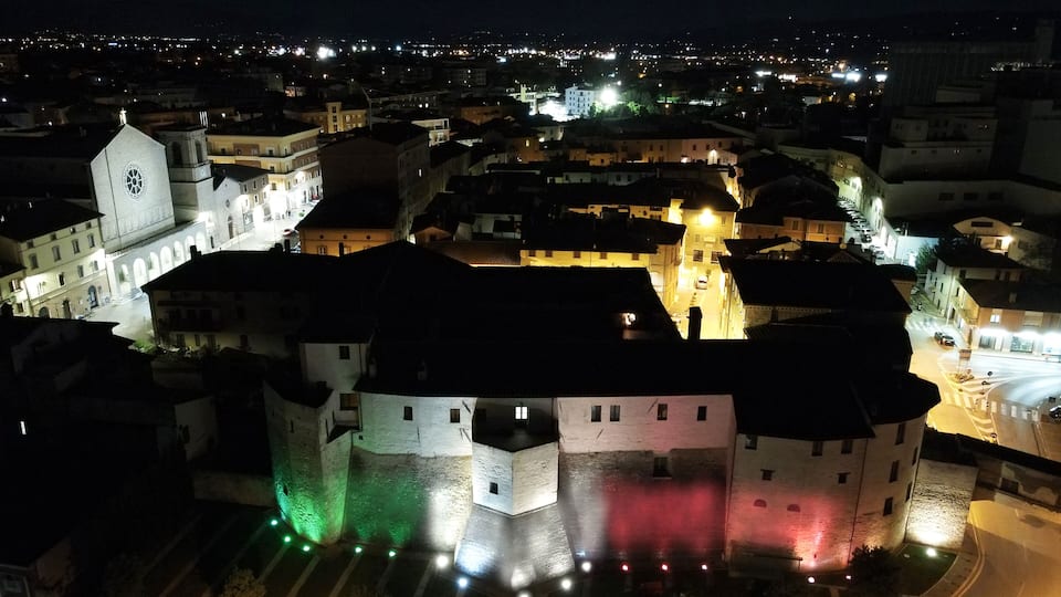 A historic castle with illuminated green and red lights, surrounded by a cityscape at night.
