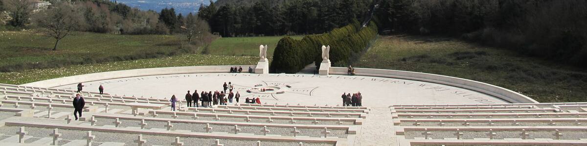 Ein großer, offener Platz mit Reihen weißer Bänke, einer Statue und einer Burg auf einem Hügel im Hintergrund.