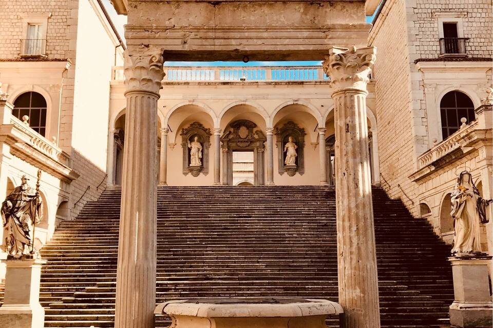 Um edifício histórico com uma fonte central, estátuas e uma cruz no topo.