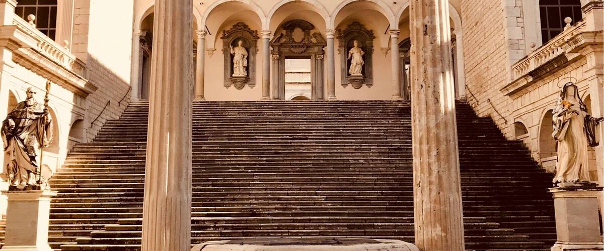 A historical building with a central fountain, statues, and a cross on top.