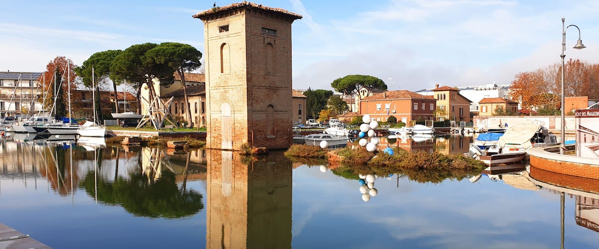 A calm waterfront with boats, a brick tower, and historic buildings.
