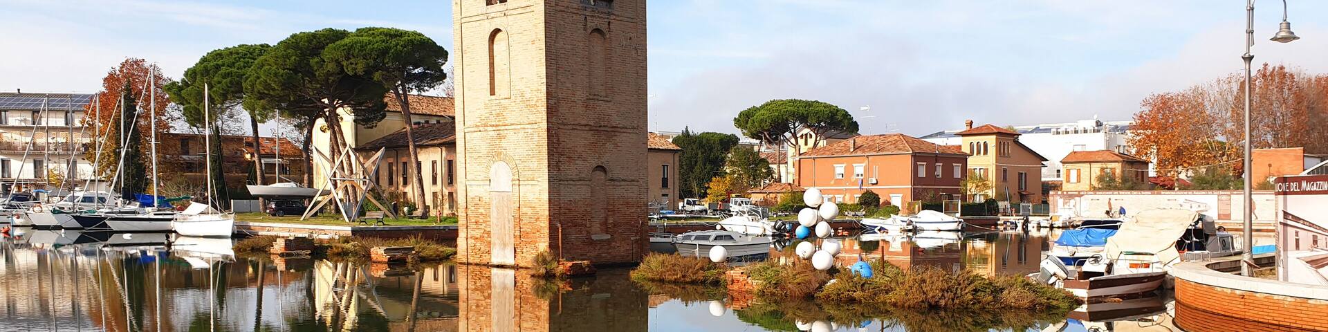 A calm waterfront with boats, a brick tower, and historic buildings.