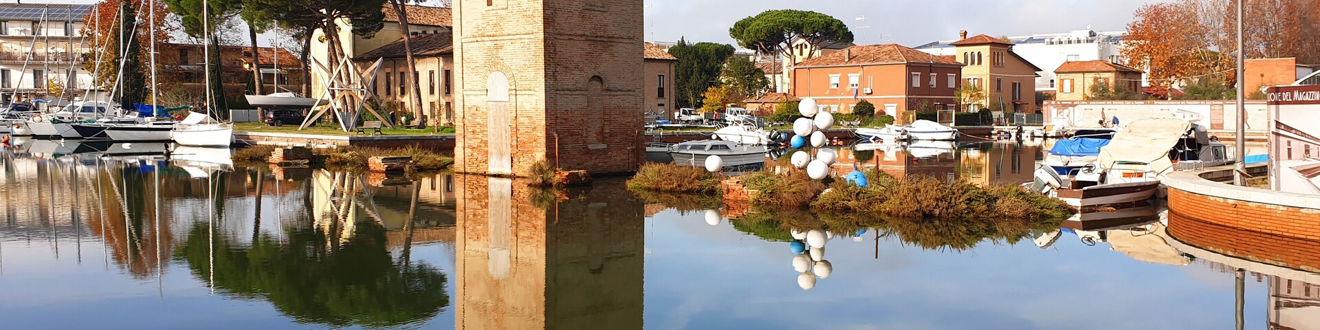 A calm waterfront with boats, a brick tower, and historic buildings.