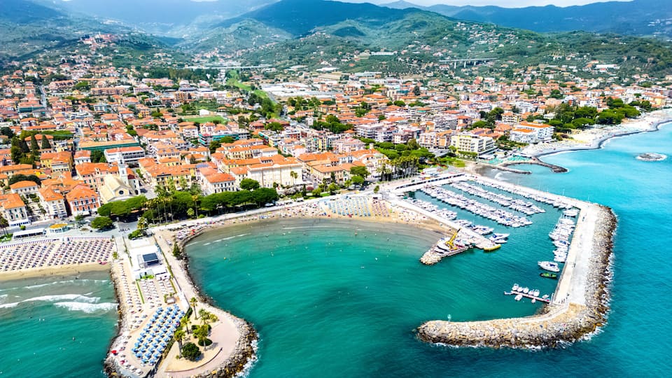 A coastal town with a marina, beach, and mountainous backdrop.