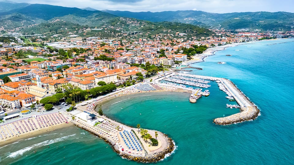 A coastal town with a marina, beach, and mountainous backdrop.