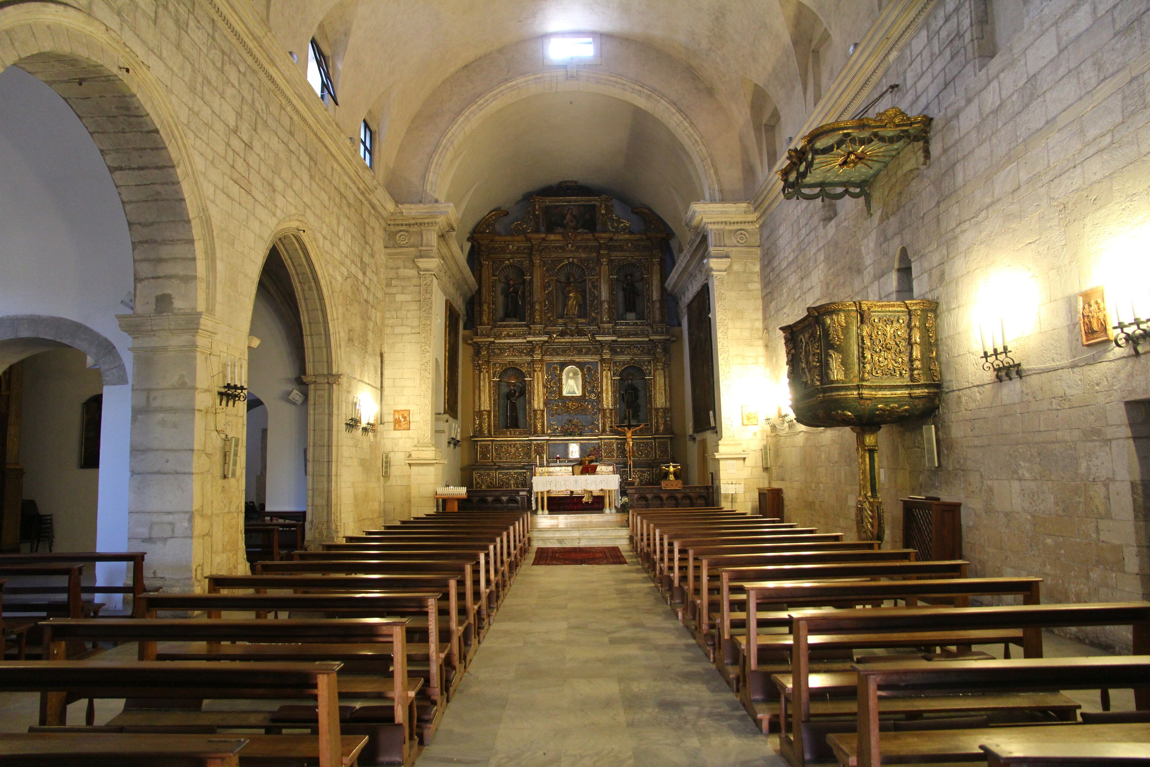 An interior of a church with arched ceilings, wooden pews, and an ornate altar.