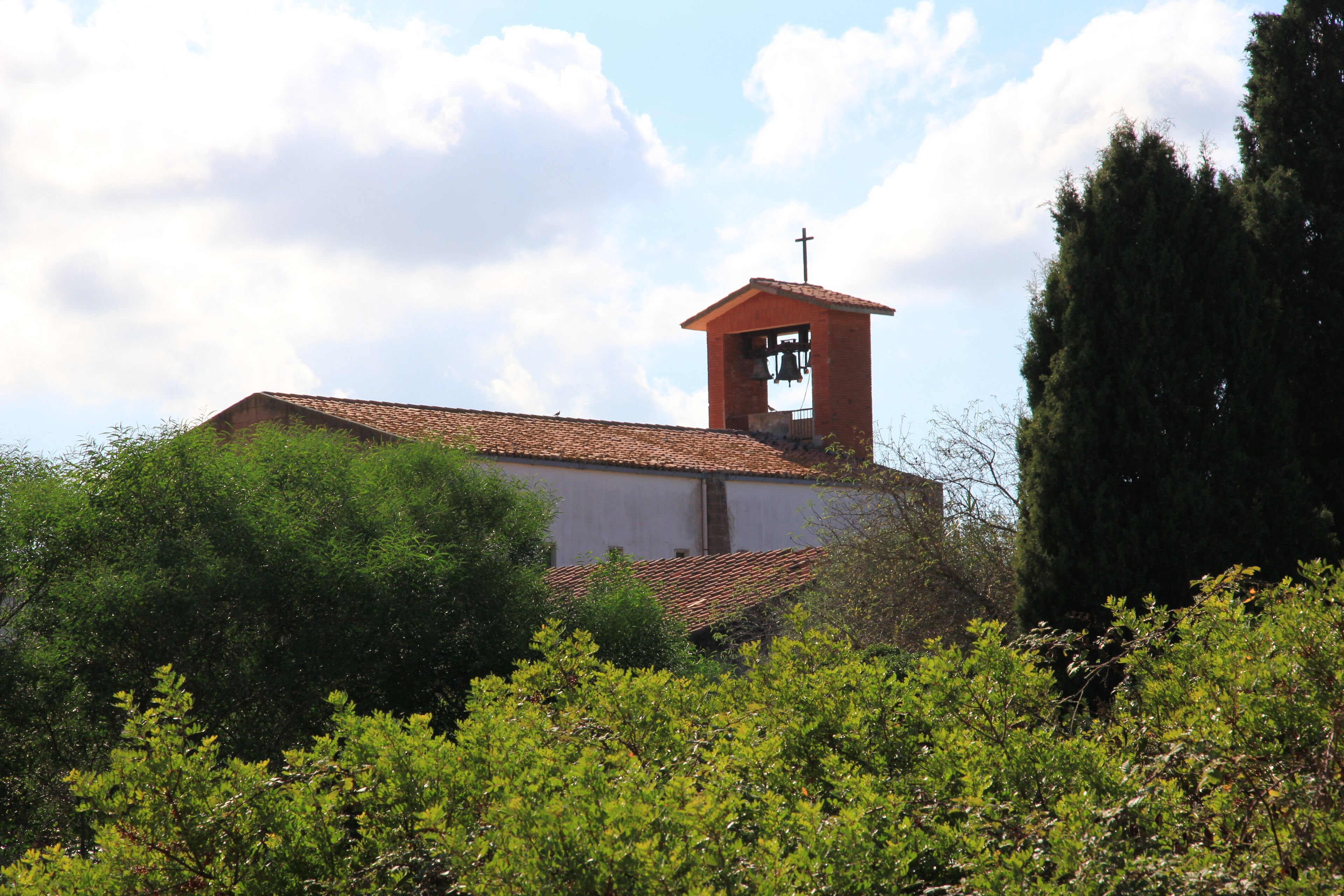 A church with a bell tower and cross, surrounded by greenery.