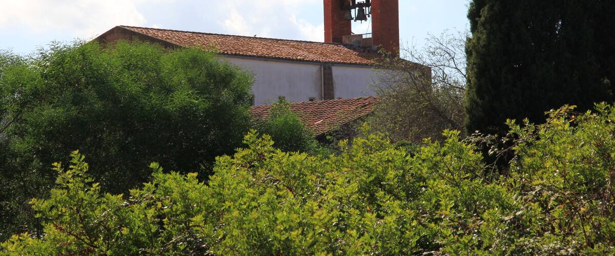 A church with a bell tower and cross, surrounded by greenery.
