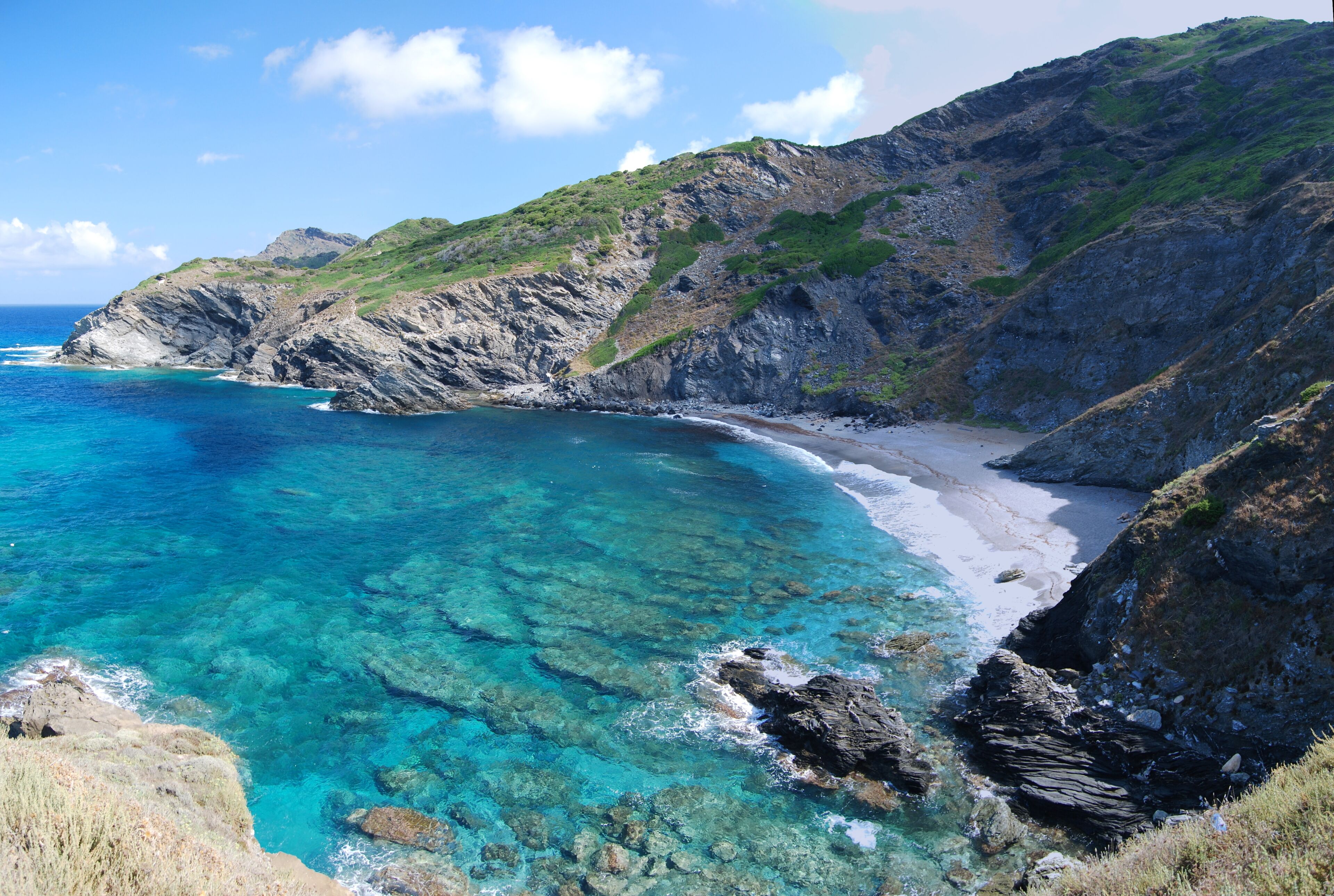 A coastal landscape with clear turquoise waters, rocky cliffs, and a sandy beach.