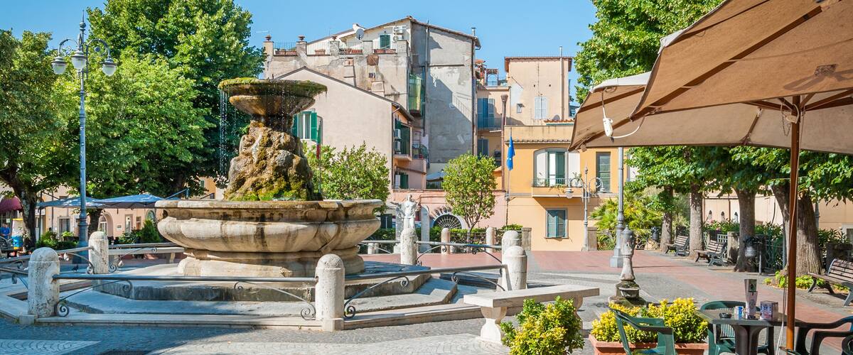 A fountain in a square surrounded by buildings and trees.