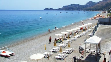 A beach with clear blue water, sun loungers, umbrellas, and boats.