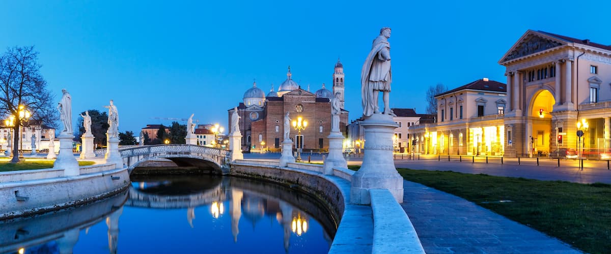 A canal with statues, a bridge, and illuminated buildings at dusk.