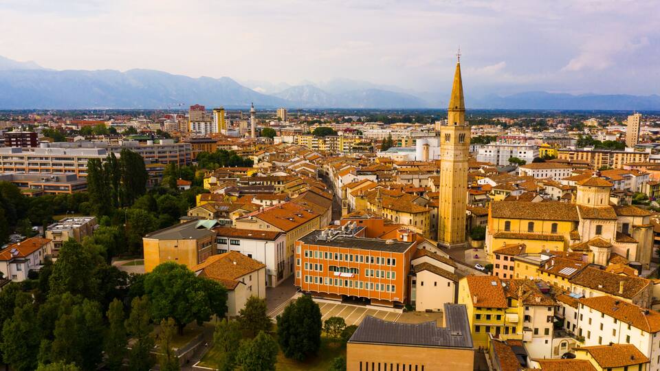 A cityscape with a prominent church tower, surrounded by historic buildings and a mountainous backdrop.