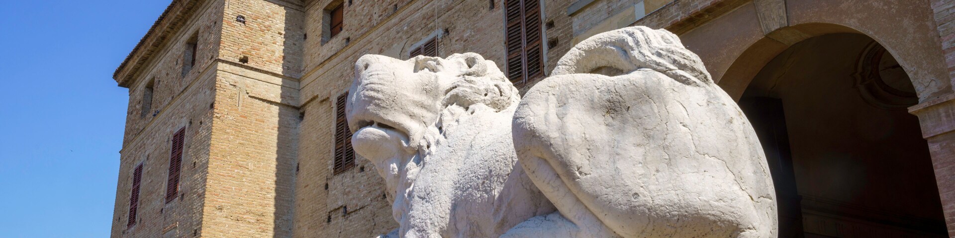 Una estatua de león de piedra frente a un edificio histórico con ventanas de arco y tejado de tejas.