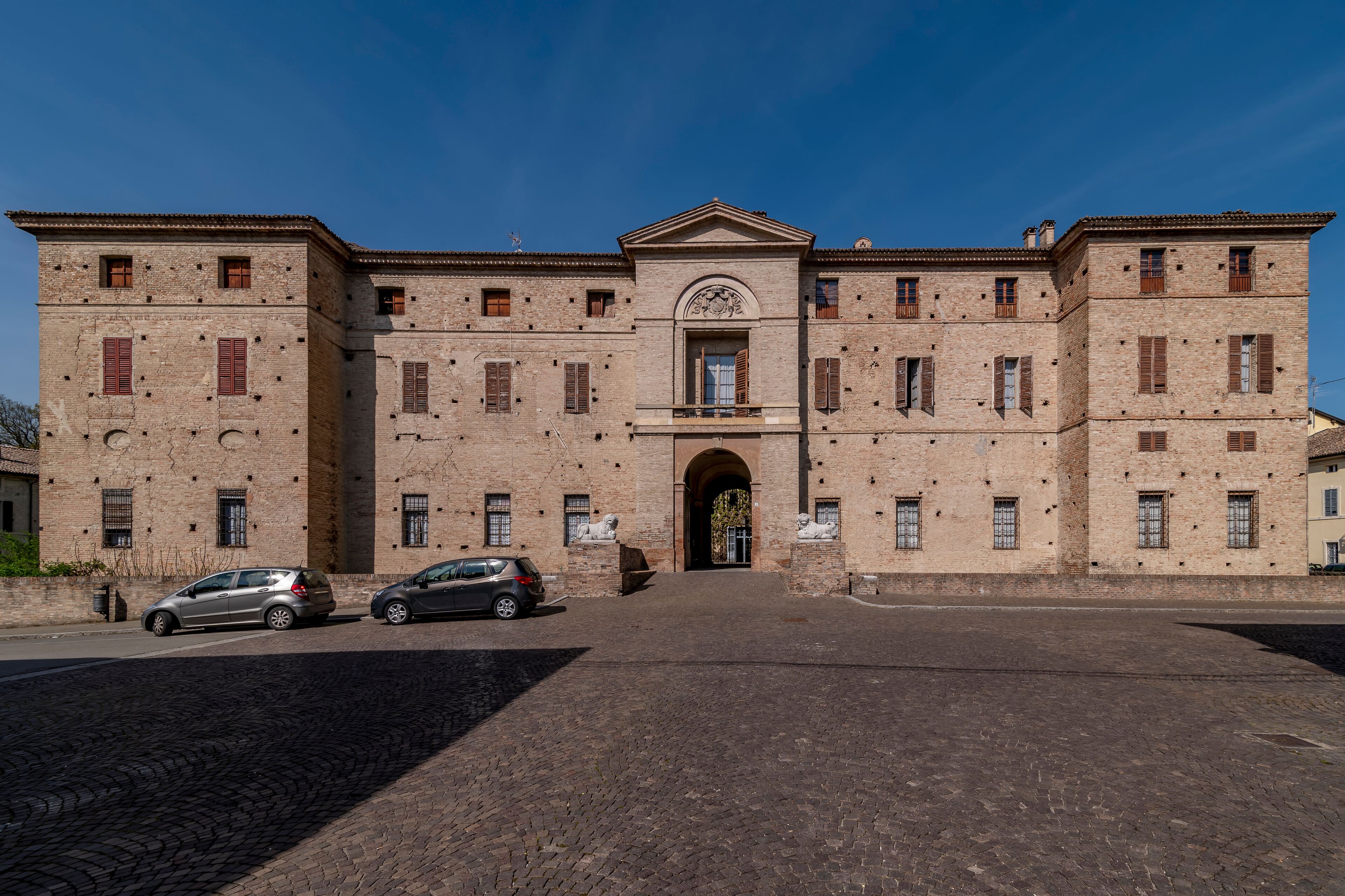 A historic building with a central archway, multiple windows, and a paved courtyard.