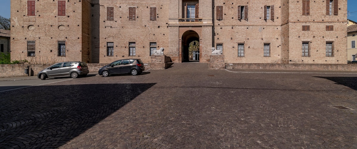 A historic building with a central archway, multiple windows, and a paved courtyard.